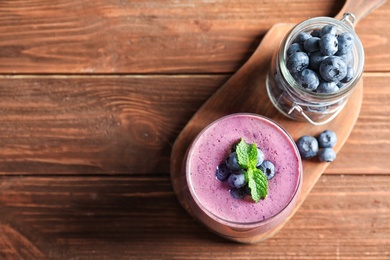 Photo of Glass of smoothie and jar with blueberries on wooden background, top view. Space for text