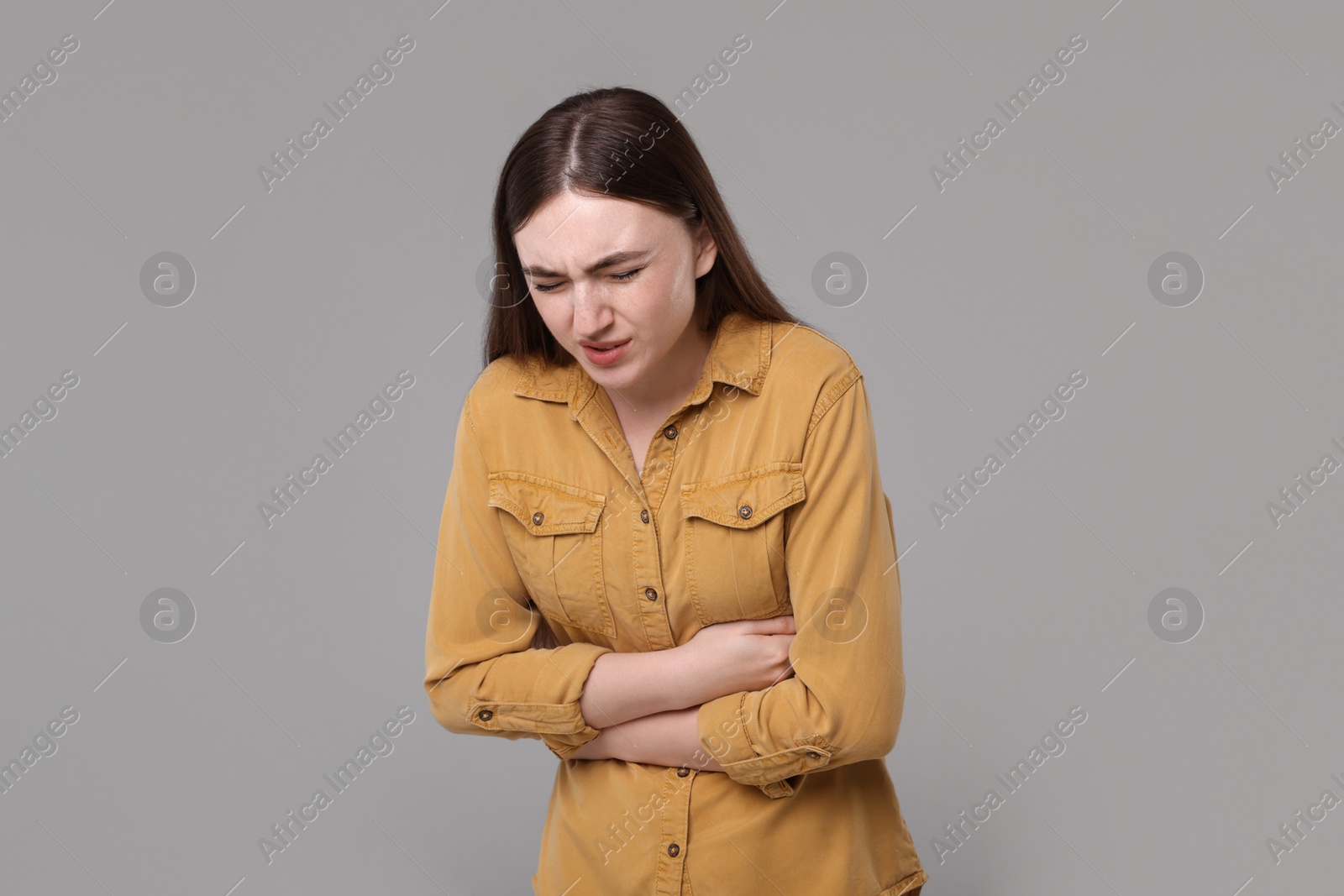 Photo of Young woman suffering from stomach pain on grey background