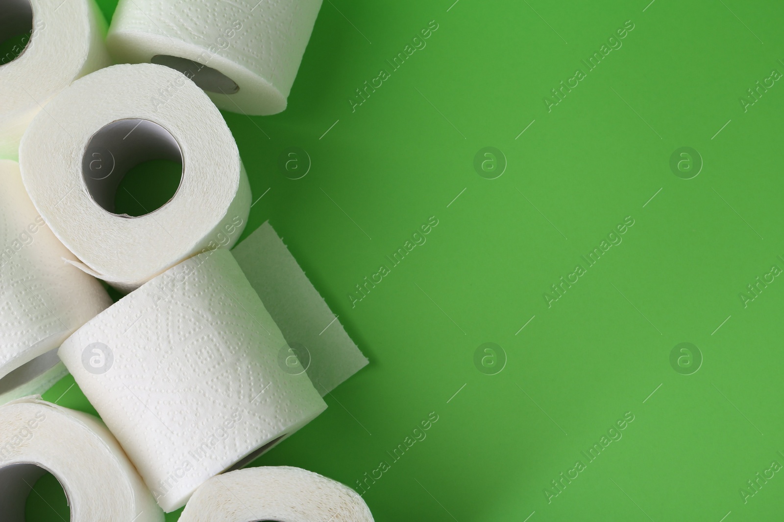 Photo of Soft toilet paper rolls on green background, flat lay. Space for text