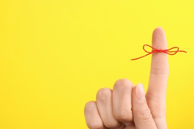 Woman showing index finger with tied red bow as reminder on yellow background, closeup. Space for text