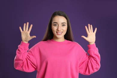 Woman showing number ten with her hands on purple background
