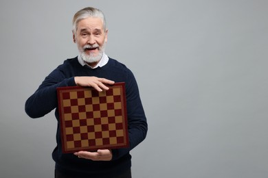 Emotional man with chessboard on light gray background, space for text