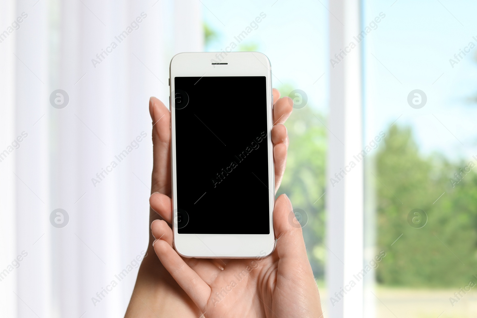 Photo of Woman holding smartphone with blank screen on blurred background. Mockup for design