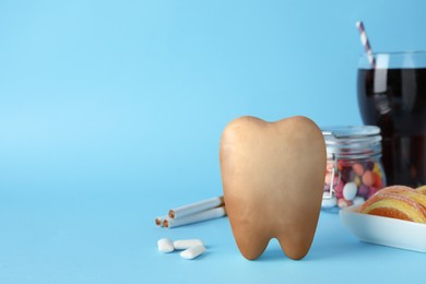 Photo of Tooth model with cute face, gums and harmful products on light blue background. Space for text