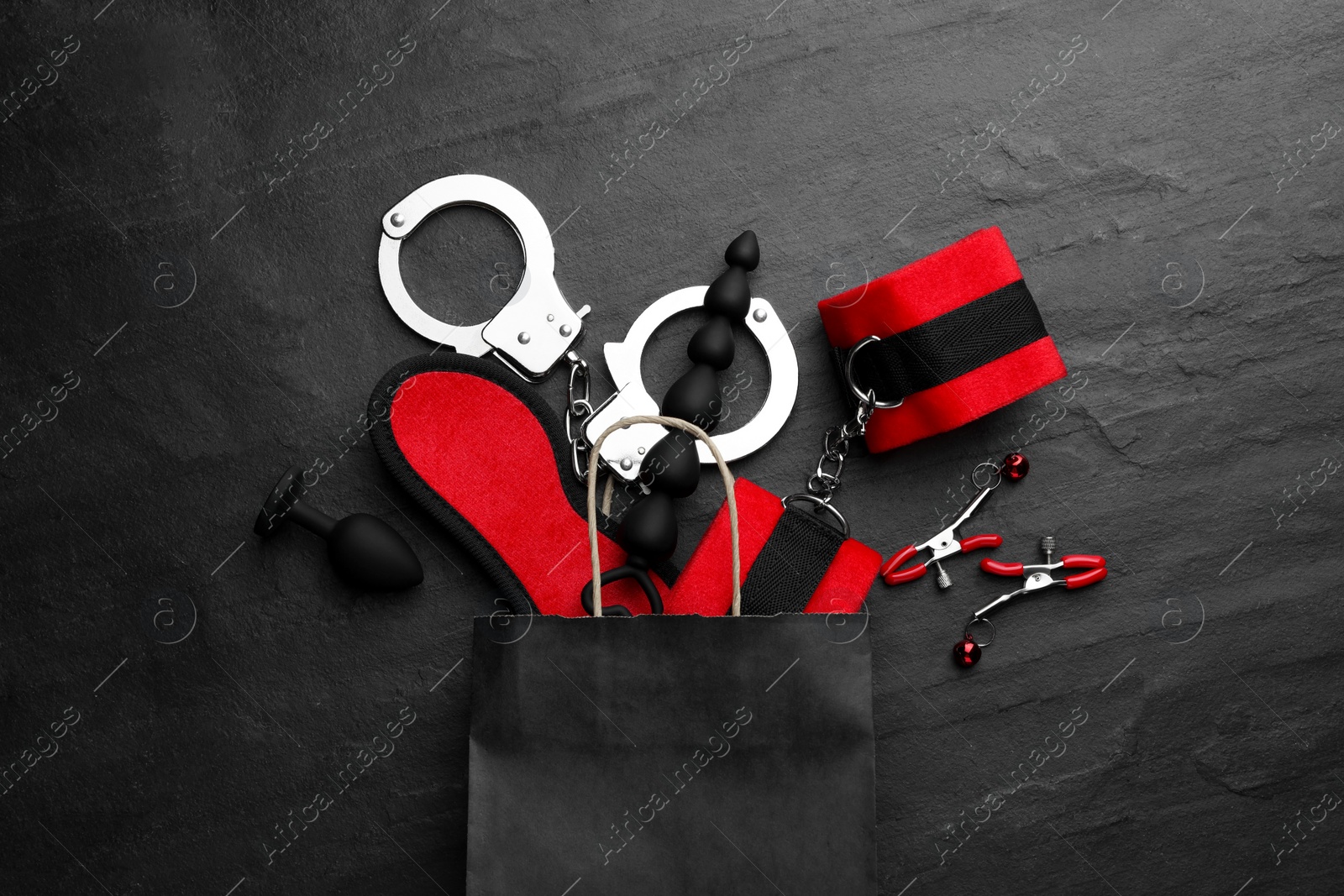 Photo of Paper shopping bag with different sex toys on black table, flat lay