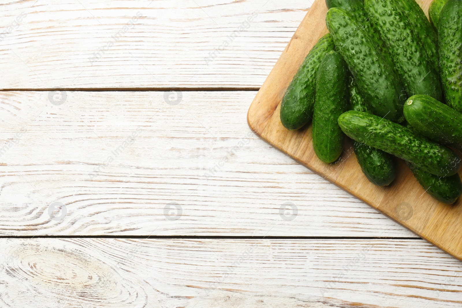 Photo of Fresh ripe cucumbers on white wooden table, top view. Space for text