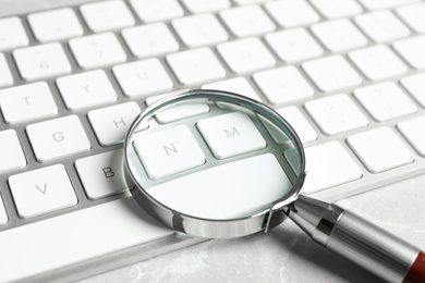 Photo of Magnifying glass and computer keyboard on light grey marble table, closeup. Search concept