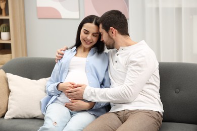 Photo of Happy pregnant woman with her husband on sofa at home