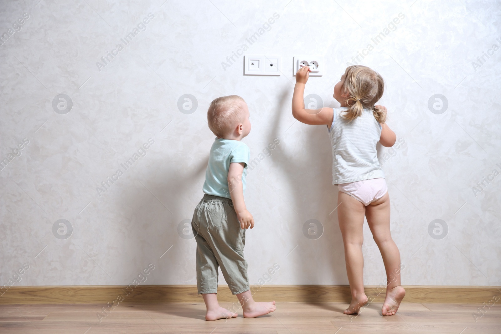 Photo of Little children playing with electrical socket indoors, space for text. Dangerous situation