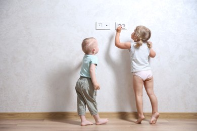 Little children playing with electrical socket indoors, space for text. Dangerous situation