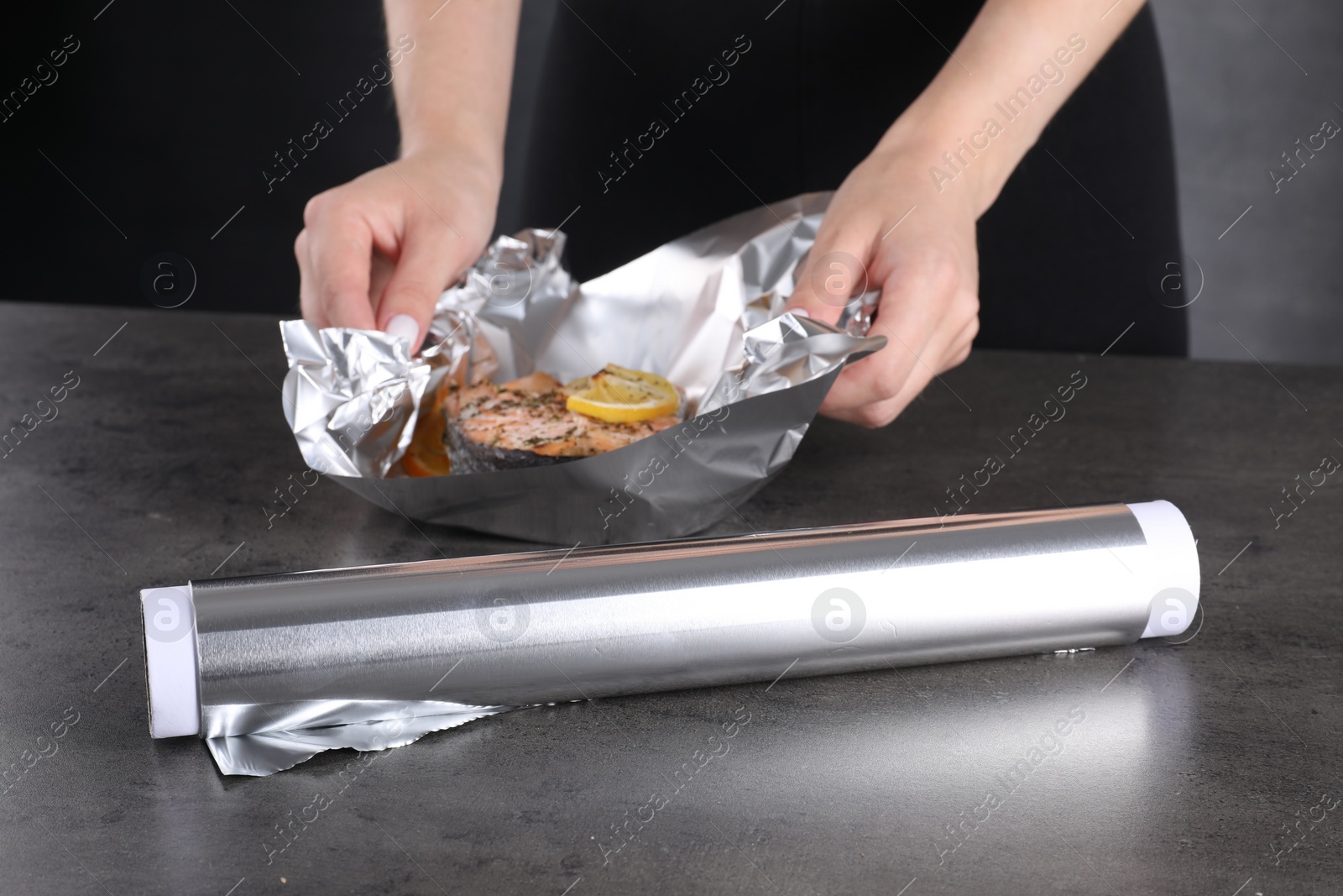 Photo of Aluminum foil and woman with tasty salmon at grey textured table, closeup