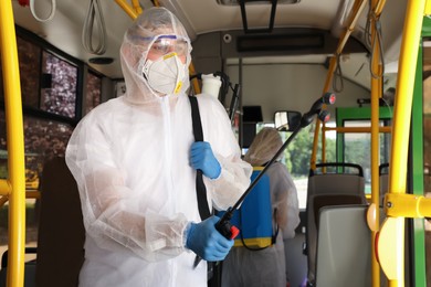 Public transport sanitation. Workers in protective suits disinfecting bus salon