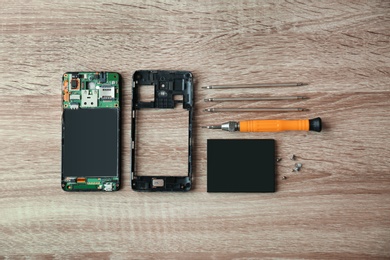 Flat lay composition with disassembled mobile phone and tools on wooden table. Repairing service