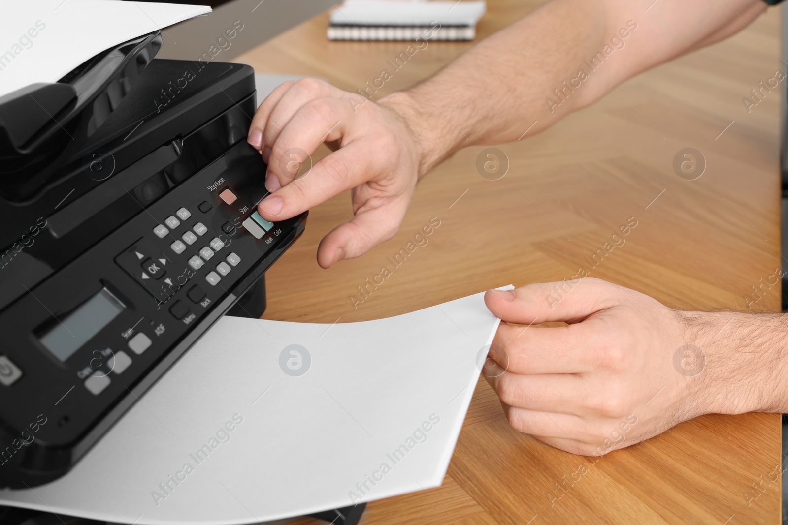 Photo of Man using modern printer at wooden table indoors, closeup