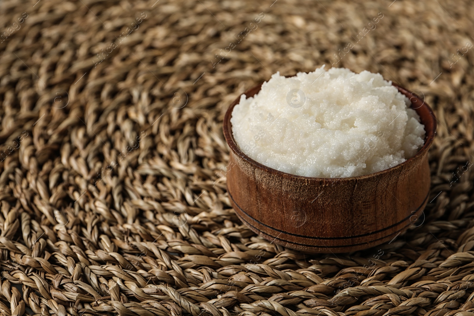 Photo of Shea butter in bowl on wicker mat, closeup. Space for text