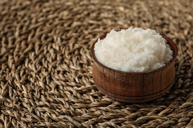 Photo of Shea butter in bowl on wicker mat, closeup. Space for text