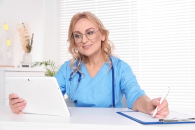 Photo of Doctor with glasses and tablet consulting patient in clinic. Online medicine concept