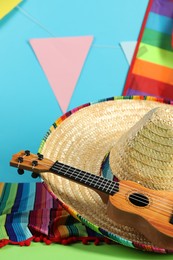 Photo of Mexican sombrero hat, poncho and ukulele on green table, closeup