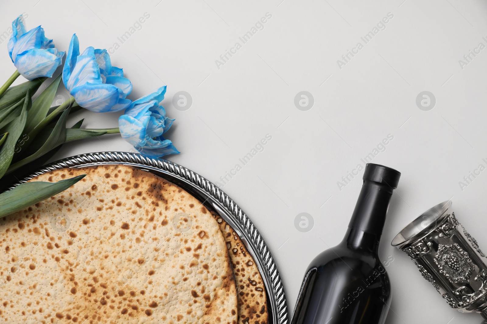 Photo of Tasty matzos, wine and tulips on light grey background, flat lay with space for text. Passover (Pesach) celebration