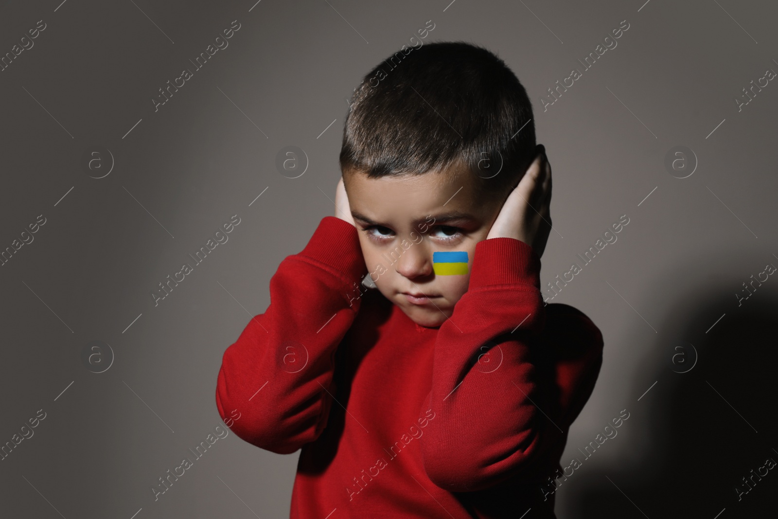 Image of Sad little boy with picture of Ukrainian flag on cheek against light background. Stop war in Ukraine