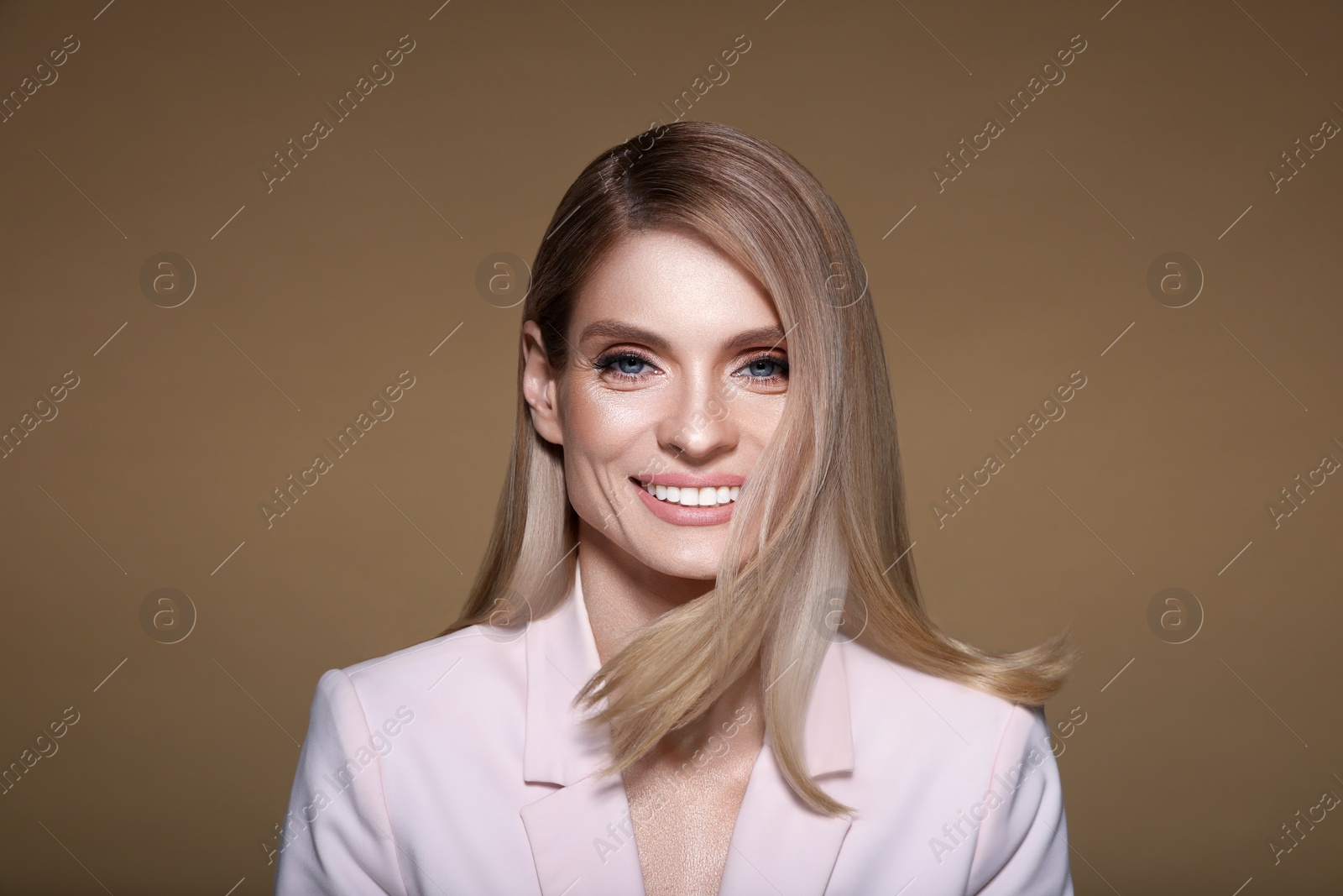 Image of Portrait of stylish attractive woman with blonde hair smiling on pastel brown background