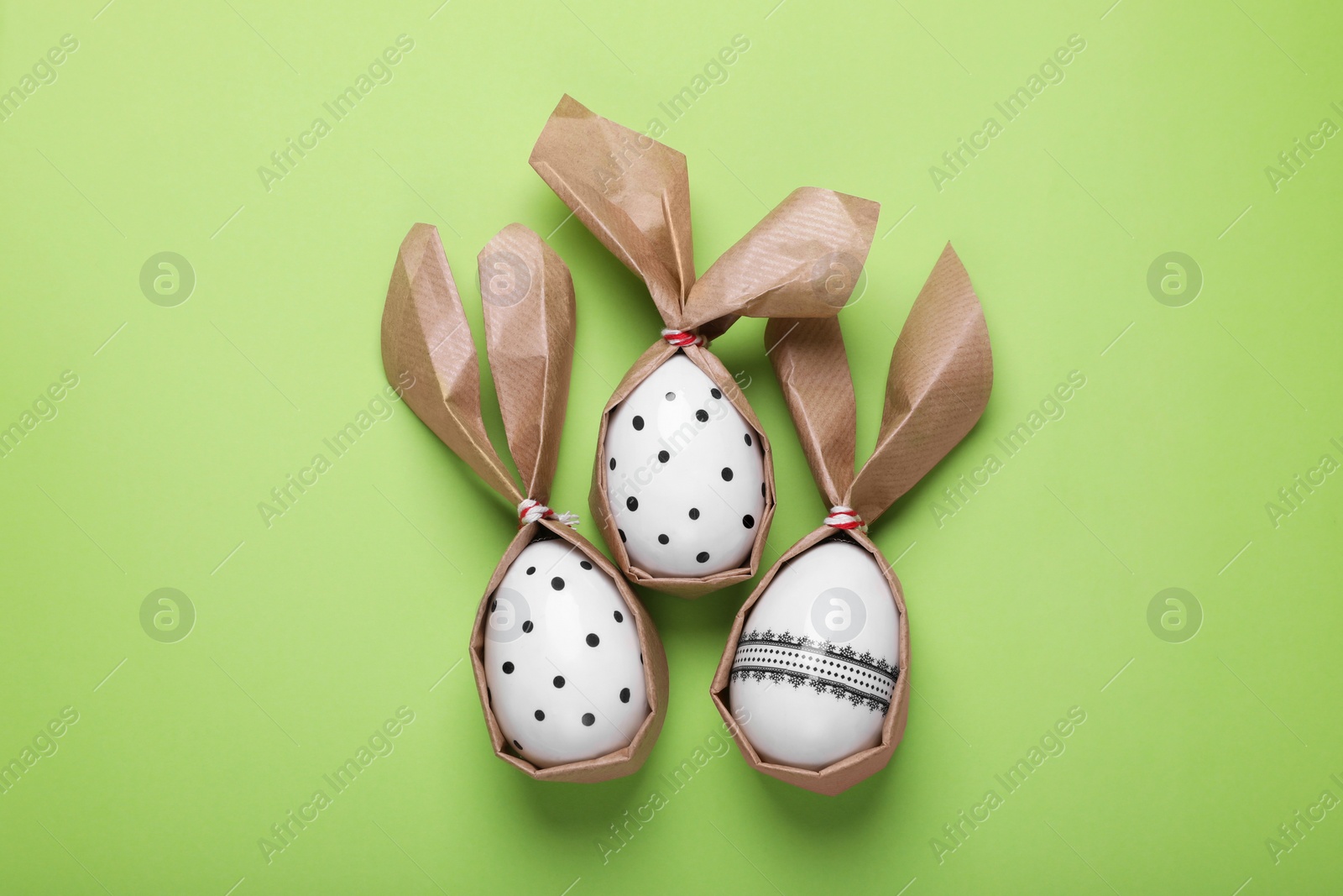 Photo of Easter bunnies made of craft paper and eggs on light green background, flat lay