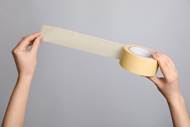 Photo of Woman holding beige adhesive tape on light grey background, closeup