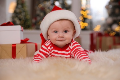 Cute little baby in bright pajamas and Santa hat on floor at home. Christmas suit