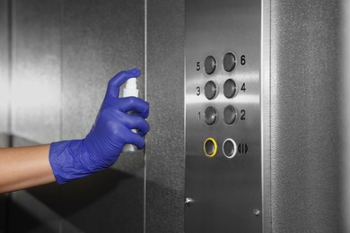 Photo of Woman cleaning buttons panel in elevator with detergent spray, closeup