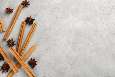 Aromatic cinnamon sticks and anise on light grey table, flat lay. Space for text