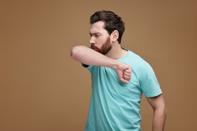 Photo of Sick man coughing into his elbow on brown background. Cold symptoms