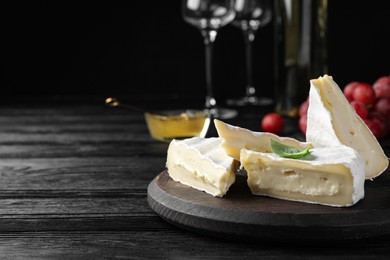Photo of Tasty brie cheese with basil on black wooden table, space for text