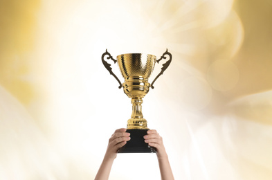 Image of Woman holding gold trophy cup on color background, closeup