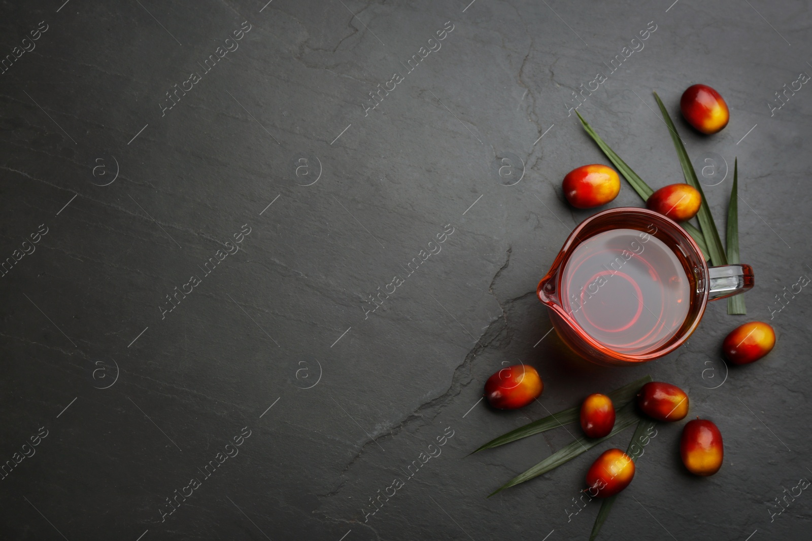 Image of Palm oil in glass jug, tropical leaf and fruits on black table, flat lay. Space for text