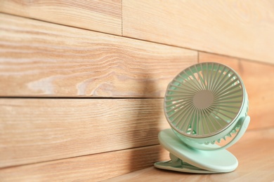 Photo of Portable fan on table near wooden wall, space for text. Summer heat