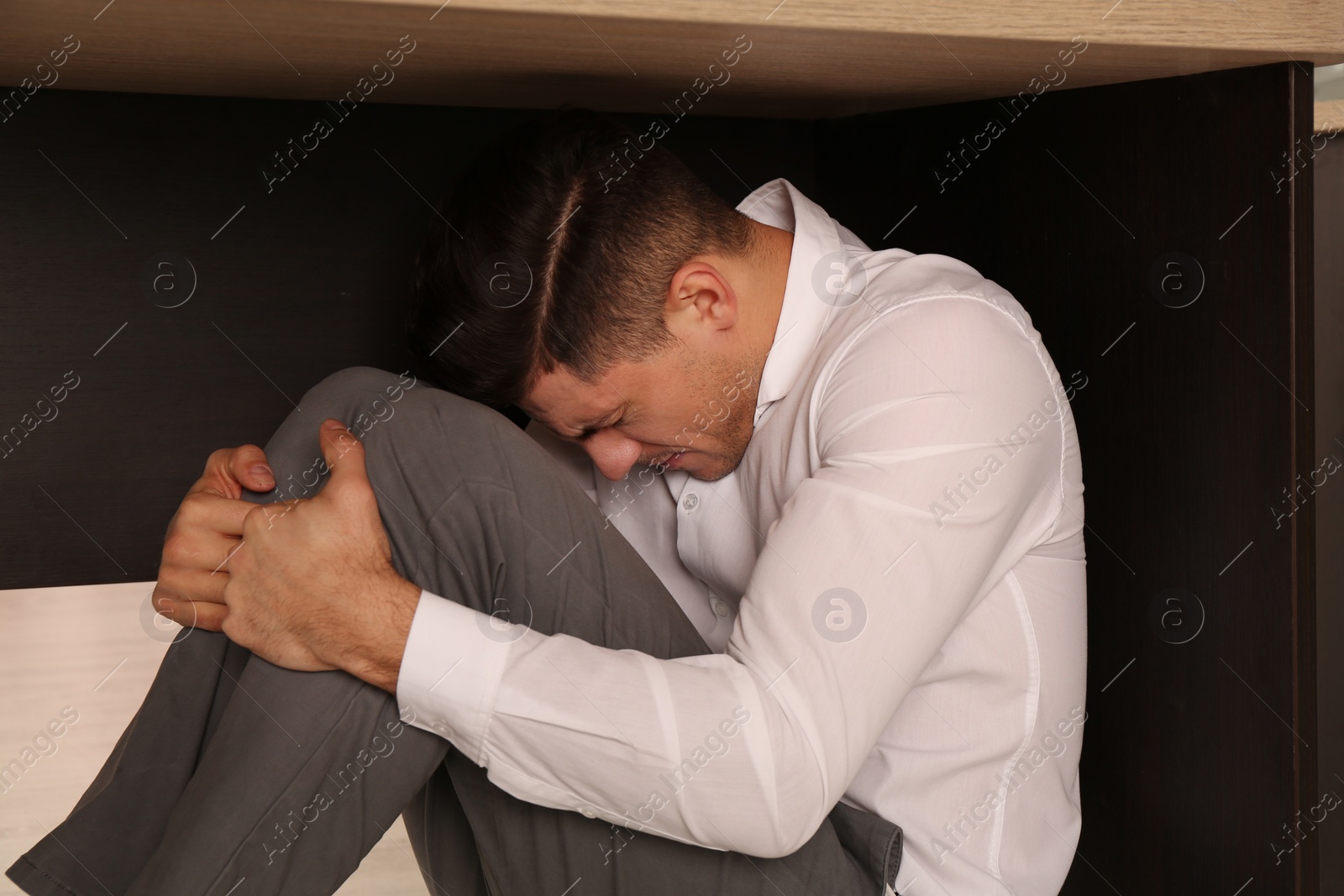 Photo of Scared man hiding under office desk during earthquake