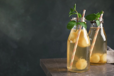 Photo of Bottles with tasty melon ball drink on table against dark background. Space for text