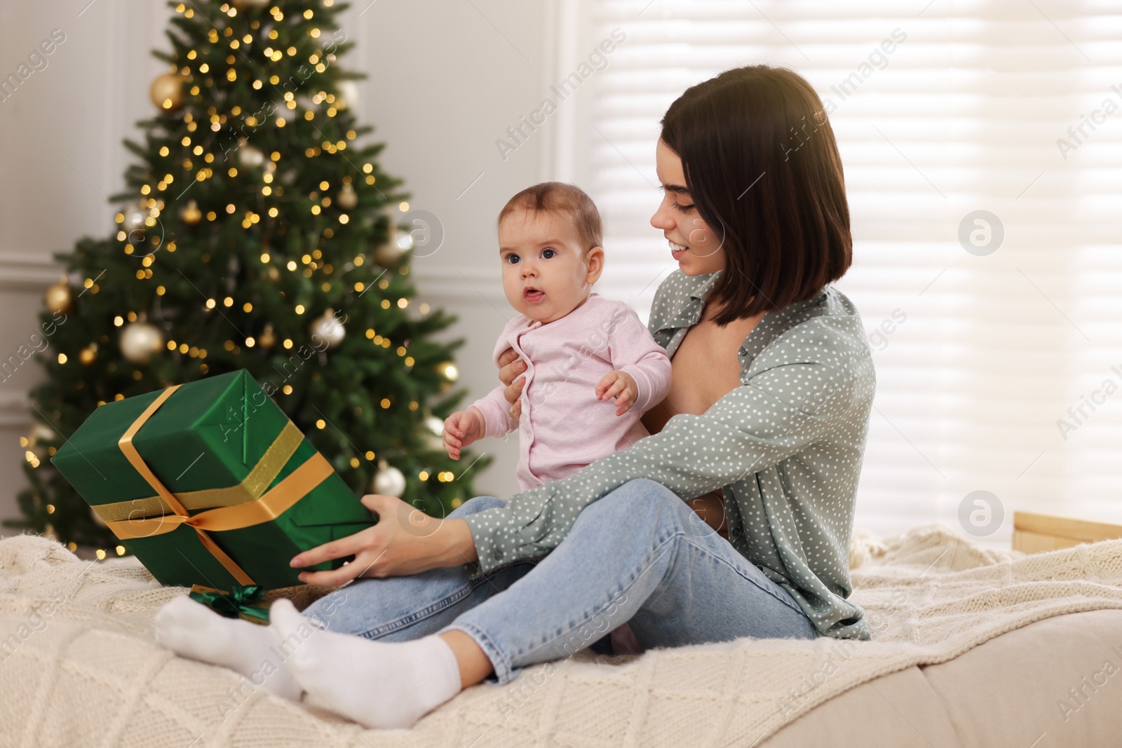 Photo of Happy young mother with her cute baby on bed in room decorated for Christmas. Winter holiday