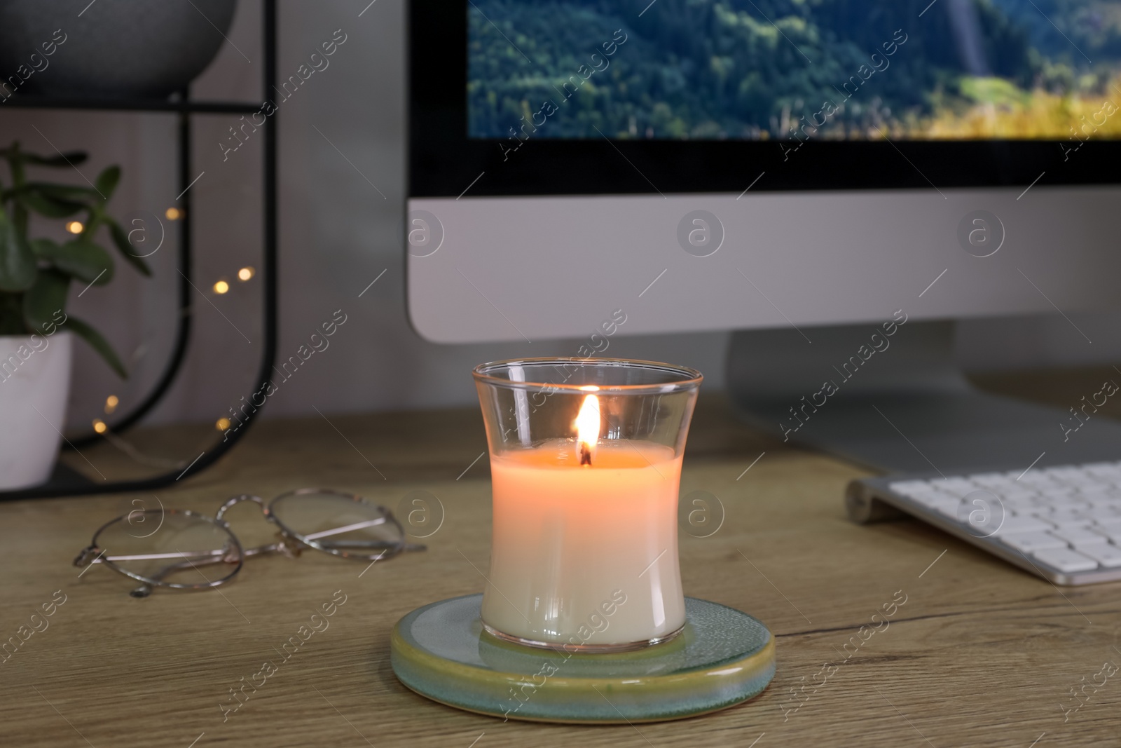 Photo of Burning candle, glasses and computer on wooden table indoors