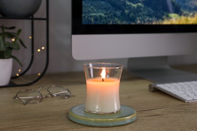 Photo of Burning candle, glasses and computer on wooden table indoors