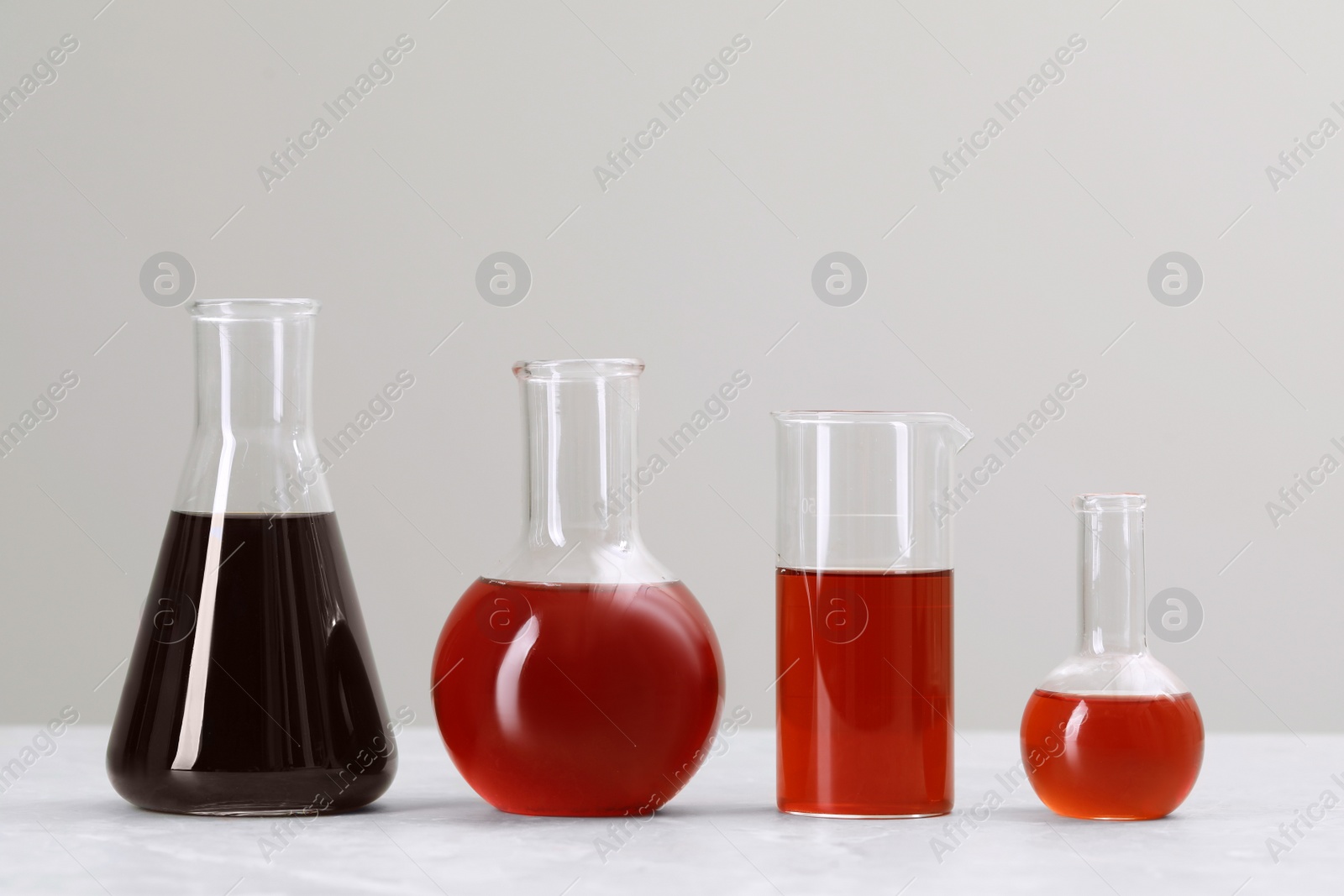 Photo of Different laboratory glassware with brown liquids on white table against light background