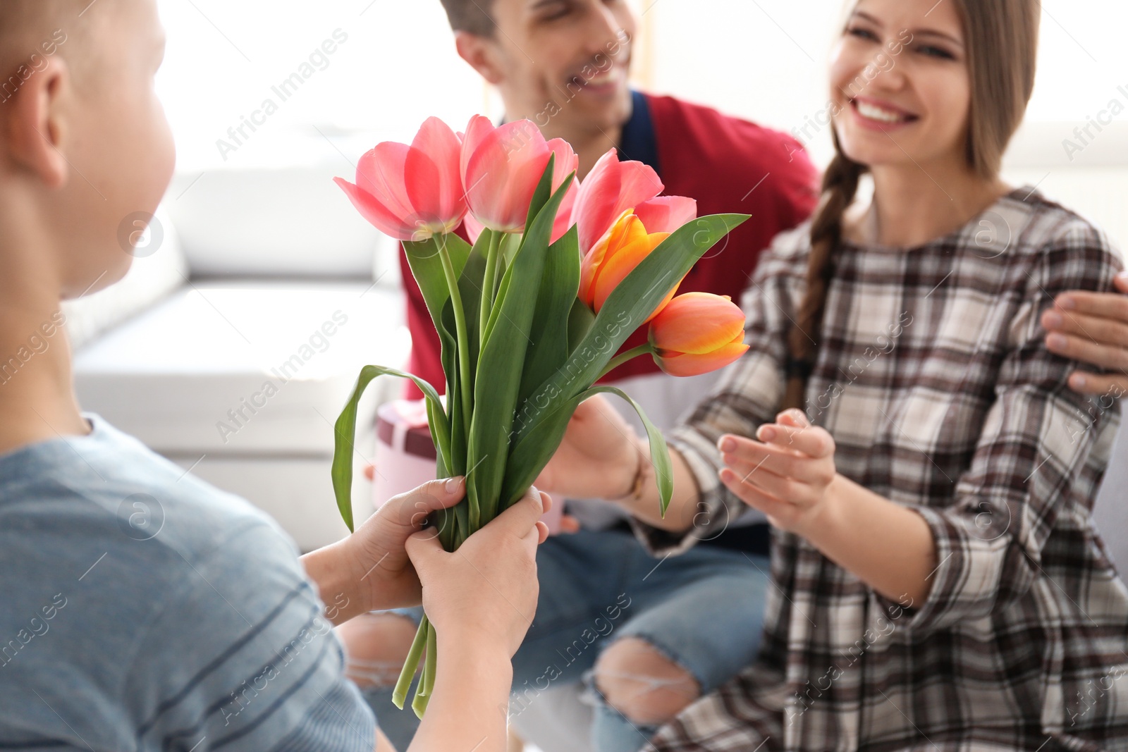 Photo of Happy woman receiving flowers and gift from her family at home. Mother's day celebration