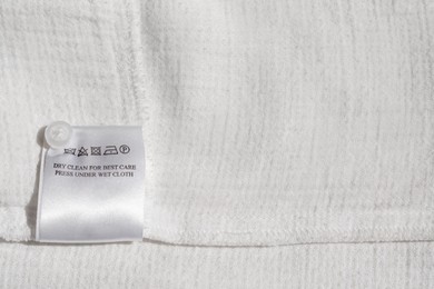Photo of Clothing label with instruction on white garment, top view. Space for text