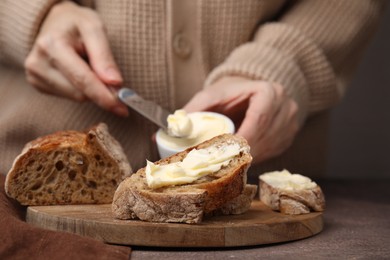 Photo of Woman spreading butter onto bread at wooden table, closeup