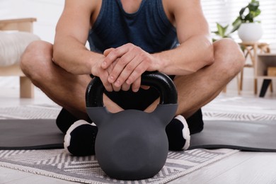 Muscular man sitting with kettlebell on mat at home, closeup