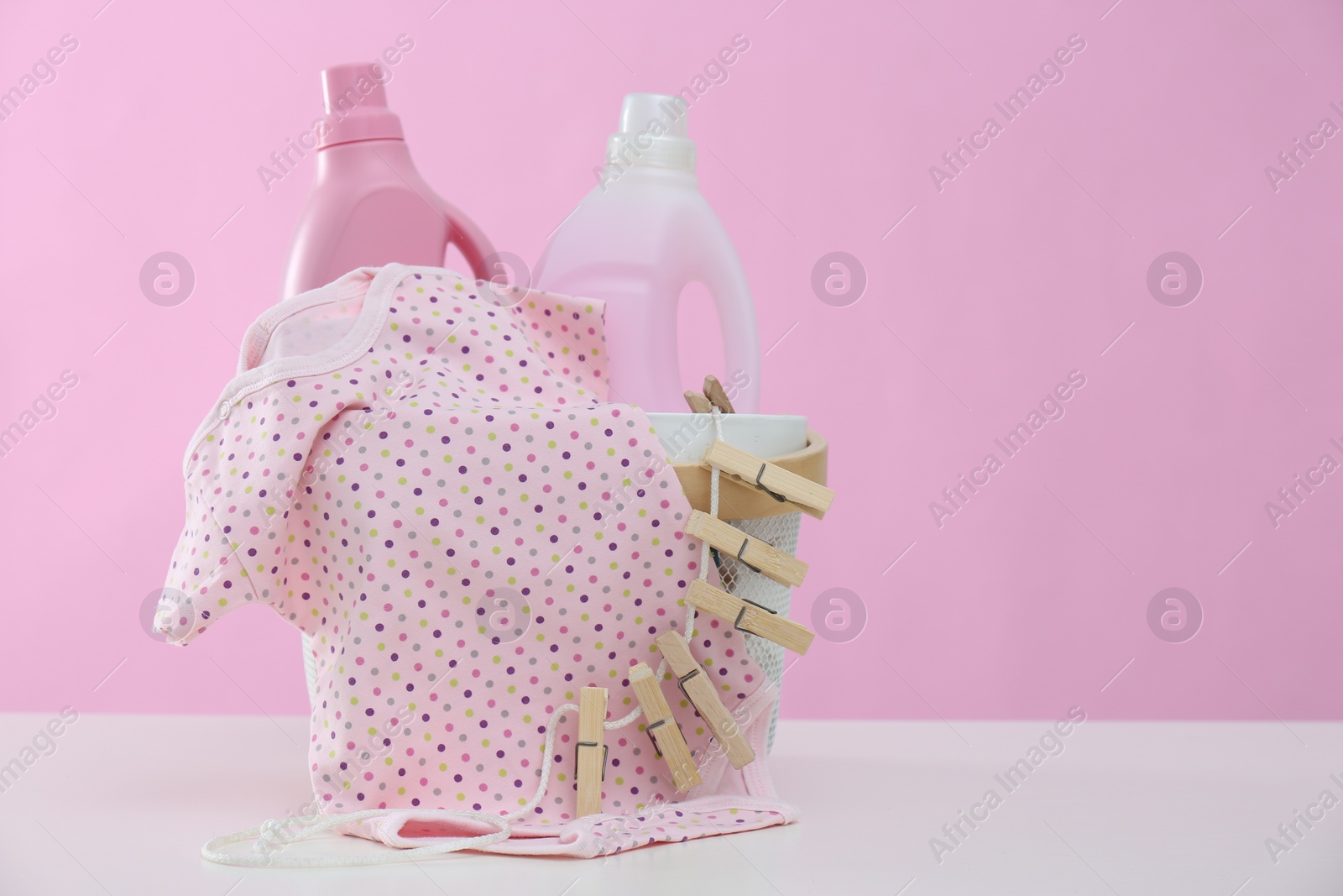 Photo of Detergents and children's clothes on white table. Space for text