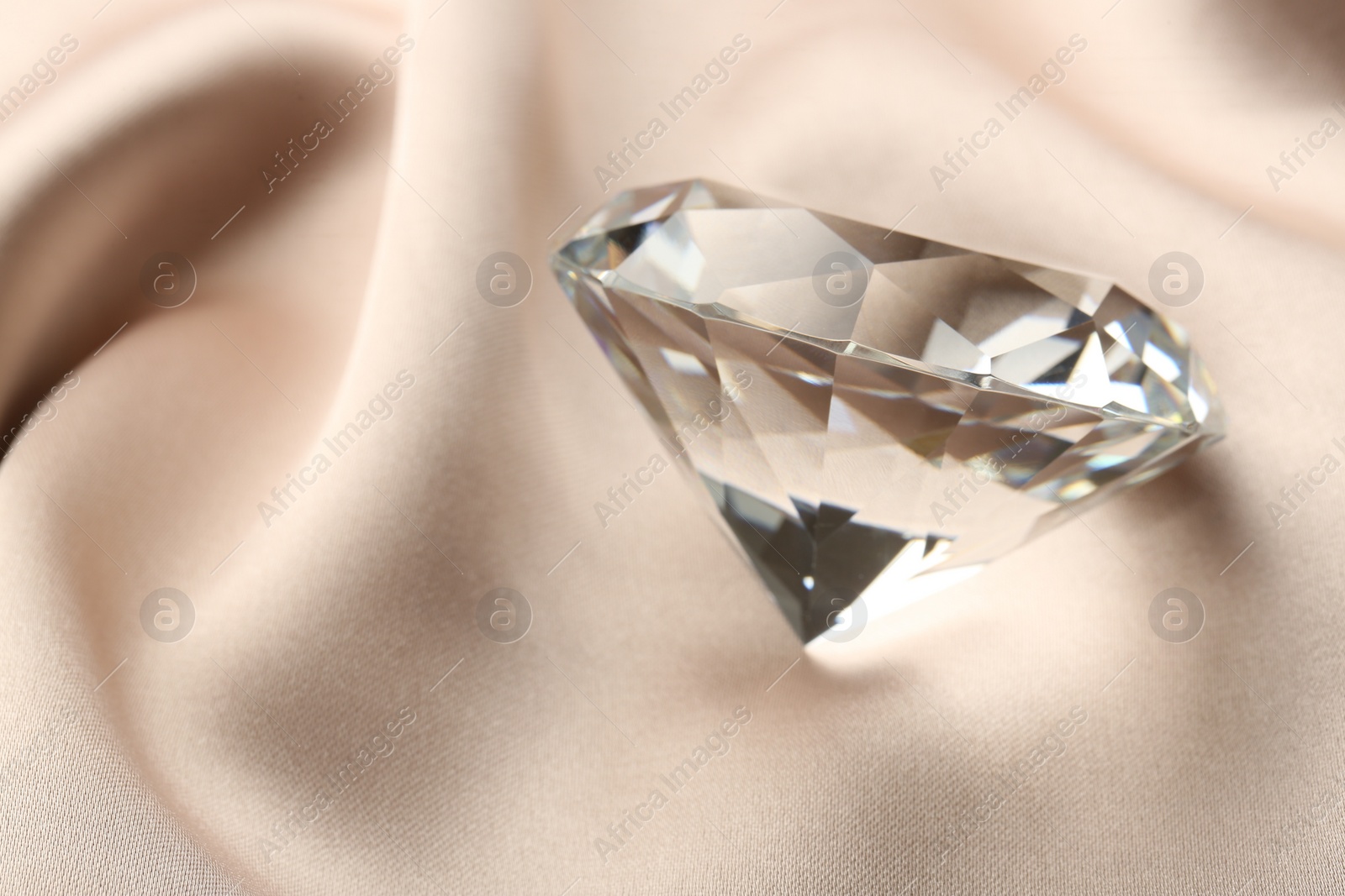 Photo of Beautiful shiny diamond on beige silky fabric, closeup. Space for text