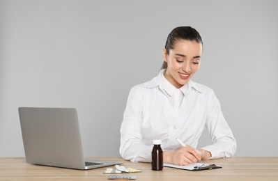 Photo of Professional pharmacist working at table against light grey background