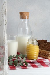 Jar with tasty honey, milk and bread on white wooden table