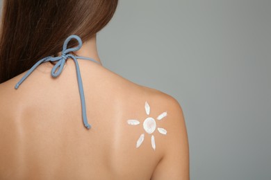 Photo of Teenage girl with sun protection cream on her back against grey background. Space for text
